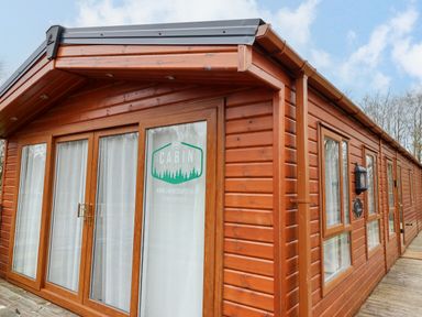 Exterior view of a wooden cabin with glass doors and windows surrounded by trees at Felmoor Park