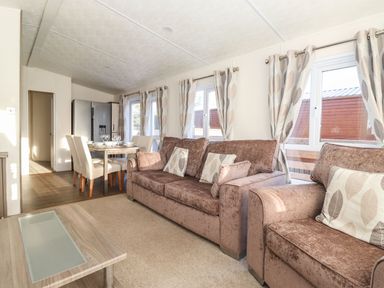 A living area with brown sofas and patterned curtains next to a dining table with chairs and a refrigerator at Canis in Felmoor Park