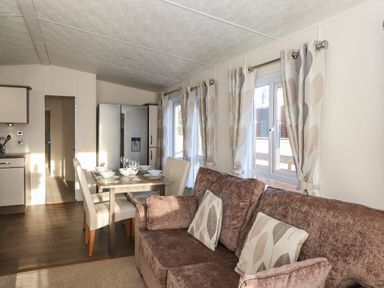 A living room with a brown sofa and dining table next to windows with leaf patterned curtains at Canis Felmoor Park