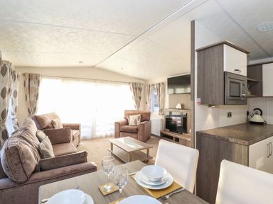 A living room with sofa, armchairs, coffee table, dining table set with plates and glasses, kitchen area, and television at Canis Felmoor Park