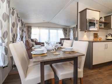 A dining table with four white chairs set with plates bowls and glasses next to a kitchen with microwave and cabinets in a living space at Canis Felmoor Park