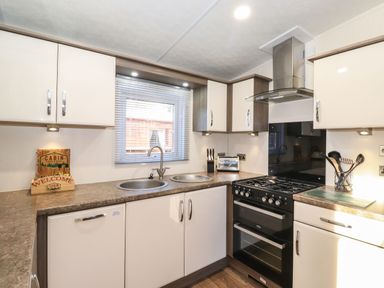 A kitchen with white cabinets a black stove two sinks a window with blinds and kitchen utensils at Canis in Felmoor Park