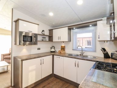 A kitchen with white cabinets a microwave stove and a double sink at Canis in Felmoor Park
