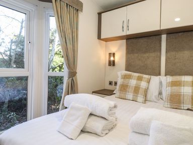 A bedroom with a double bed pillows folded towels and windows with curtains at Canis in Felmoor Park