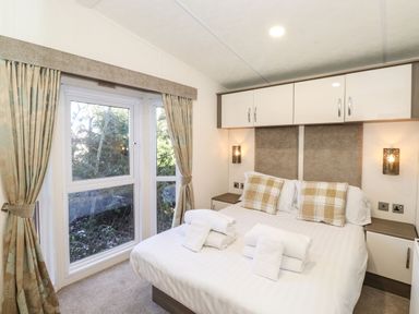 A bedroom with a double bed towels on bed bedside tables and curtains by large windows at Canis in Felmoor Park