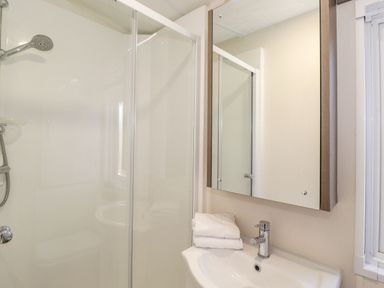 A bathroom with a shower cubicle a sink with folded towels and a mirrored cabinet at Canis in Felmoor Park