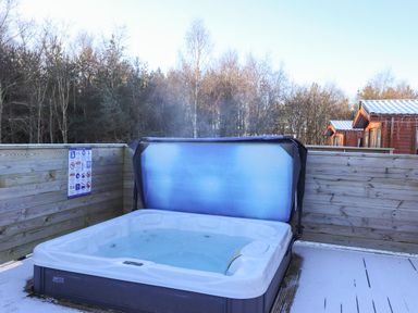 An outdoor hot tub with steam rising on a wooden deck with a partial snow cover at Canis in Felmoor Park