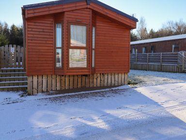 A wooden cabin with steps and a fence in a snowy outdoor setting at Canis in Felmoor Park