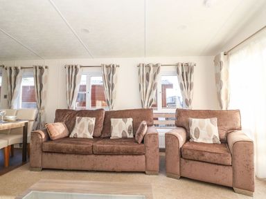 A living room with brown sofa and armchair with patterned cushions and matching curtains at Canis in Felmoor Park