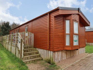 A wooden cabin with a deck and stairs surrounded by grass at Canis in Felmoor Park