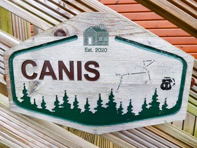 A wooden sign with the text CANIS and an engraving of a house with Est 2020 above trees and a constellation at Felmoor Park
