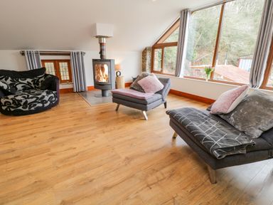 A living room with wooden floor a round patterned sofa two grey chairs with cushions a fireplace and large windows at Monkleigh Mill in Monkleigh near Bideford