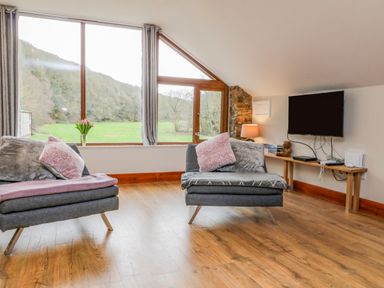 A living room with two gray armchairs and a wall-mounted television at Monkleigh Mill in Monkleigh near Bideford