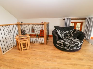 A wooden floor area with a black and patterned armchair a set of nested wooden tables and musical instruments on a railing at Monkleigh Mill in Monkleigh near Bideford