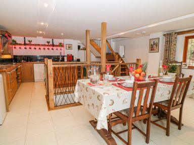 A dining area with set table and wooden chairs next to a kitchen with wooden cabinets and stairs at Monkleigh Mill in Monkleigh near Bideford