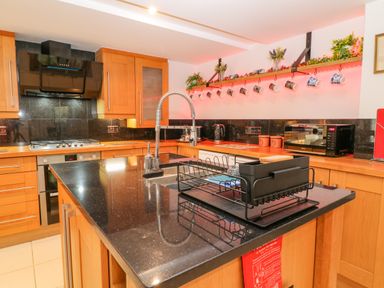 A kitchen with wooden cabinets a black countertop a sink with a flexible faucet mugs hanging on a shelf and a microwave at Monkleigh Mill Monkleigh near Bideford