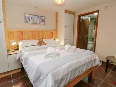 A bedroom with a double bed with rolled towels and a teddy bear a chair and a door leading to a bathroom at Monkleigh Mill in Monkleigh near Bideford