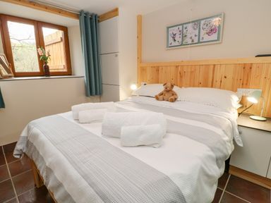 A bedroom with a bed towels a teddy bear a window with curtains and a lamp on a bedside table at Monkleigh Mill in Monkleigh near Bideford