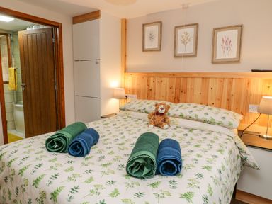 A bedroom with a double bed with floral bedding towels on the bed bedside lamps and open door to bathroom at Monkleigh Mill in Monkleigh near Bideford