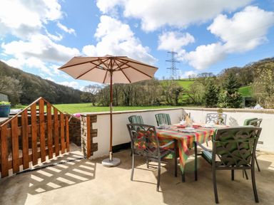 An outdoor patio area with a table covered by a checkered tablecloth and surrounded by six chairs under a large umbrella at Monkleigh Mill Monkleigh near Bideford