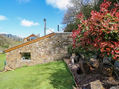 A stone building with a small window next to a garden bed with red-leaved plants at Monkleigh Mill Monkleigh near Bideford