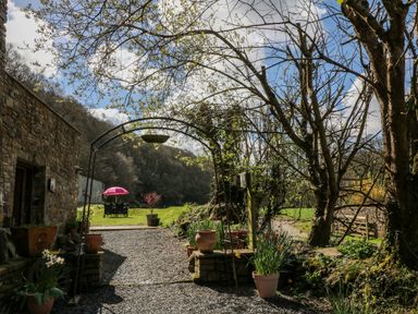 A stone building beside a gravel pathway with potted plants and a metal archway in a garden at Monkleigh Mill in Monkleigh near Bideford