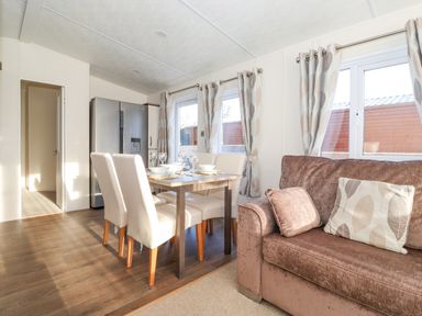A dining area with a table set for four next to a brown sofa with cushions and windows with curtains at Draco in Felmoor Park