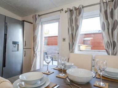 A dining area with a set table including bowls plates wine glasses and cutlery next to a refrigerator and windows with curtains at Draco in Felmoor Park