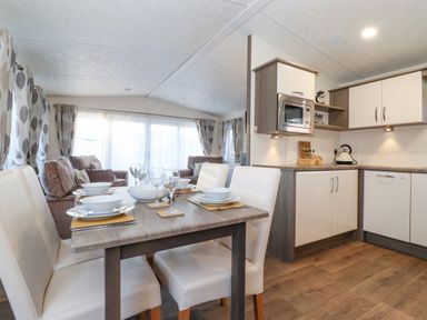 A dining table set for four next to a kitchen with cabinets and a microwave at Draco in Felmoor Park