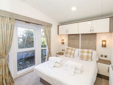 A bedroom with a double bed towels on the bed curtains and storage cabinets above the bed at Draco in Felmoor Park