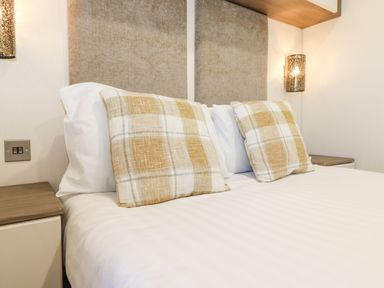 A bed with two plaid pillows and white sheets between two nightstands with wall lights at Draco in Felmoor Park