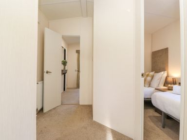 A hallway with an open door and a bedroom visible with a bed and lamp at Draco in Felmoor Park