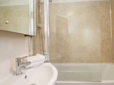 A bathroom with a white sink and faucet a folded towel a bathtub with glass shower screen and tiled walls at Draco in Felmoor Park
