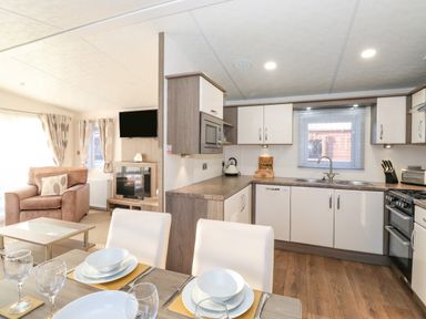 A kitchen and dining area with white cabinets and set table next to a living room with armchair and television at Ursa in Felmoor Park
