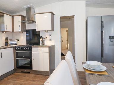 A kitchen with stove toaster refrigerator and dining table with white chairs at Ursa Felmoor Park