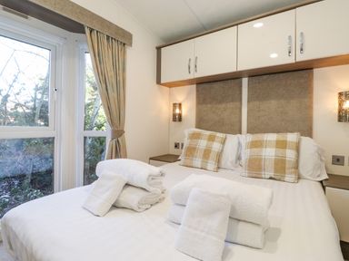 A bedroom with a double bed two plaid pillows folded white towels on the bed bedside cabinets and windows with curtains at Ursa in Felmoor Park