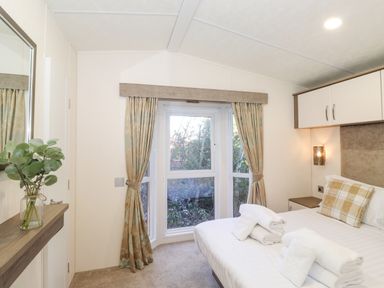 A bedroom with a bed towels a window with curtains and a small shelf with a plant at Ursa in Felmoor Park