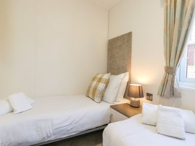 A bedroom with two single beds a bedside table with a lamp and a window with curtains at Ursa in Felmoor Park