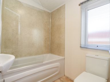 A bathroom with a bathtub a glass shower screen a toilet and a window with blinds at Ursa in Felmoor Park