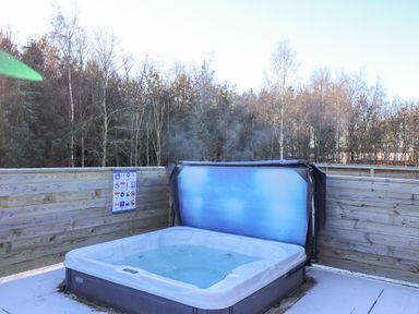 A hot tub with steam rising on a wooden deck surrounded by a wooden fence and trees at Ursa in Felmoor Park