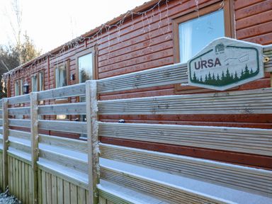 A wooden cabin with a wooden fence and a sign reading URSA at Felmoor Park