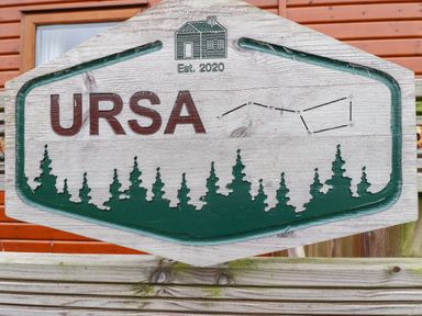 A wooden sign with the text Ursa established 2020 with tree silhouettes and a house image at Felmoor Park