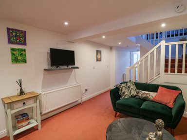 A living room with a green sofa and cushions a small table with books and a diffuser a wall mounted tv and stairs with white railings at 83 Upper John Street in Wexford Town County Wexford
