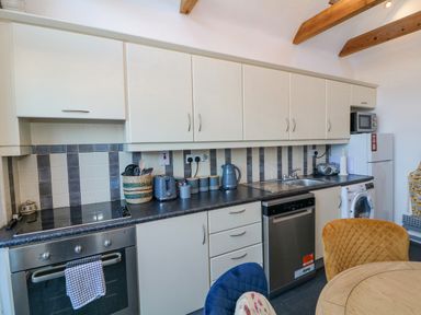 A kitchen with white cabinets a black countertop a stainless steel oven dishwasher and washing machine with a round wooden table and colored chairs at 83 Upper John Street in Wexford Town County Wexford