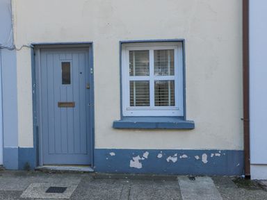 A blue front door and a window with white shutters on a cream wall with blue trim at 83 Upper John Street in Wexford Town County Wexford