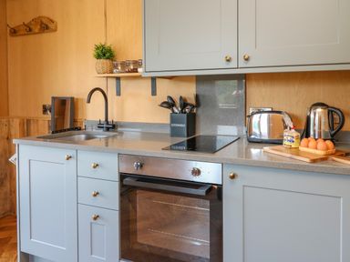 A kitchen countertop with a sink, stovetop, oven, utensils holder, toaster, kettle, and eggs on a cutting board at Rooster's Rest in Rhaedr Gwy near Rhayader