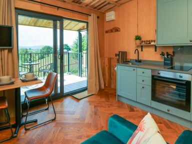 A kitchen and dining area with a sliding glass door leading to a balcony overlooking greenery at Rooster's Rest in Rhaedr Gwy near Rhayader