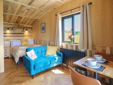 A room with a bed a blue sofa a wooden dining table with two place settings and a window with curtains at Rooster's Rest in Rhaedr Gwy near Rhayader