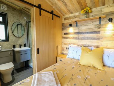 A bedroom with a double bed yellow bedding and an adjacent bathroom with a sink and toilet at Rooster's Rest in Rhaedr Gwy near Rhayader