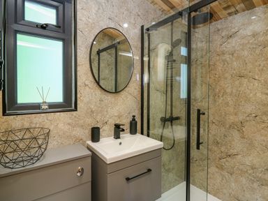 A bathroom with a shower area a sink cabinet an oval mirror and a frosted window at Rooster's Rest in Rhaedr Gwy near Rhayader